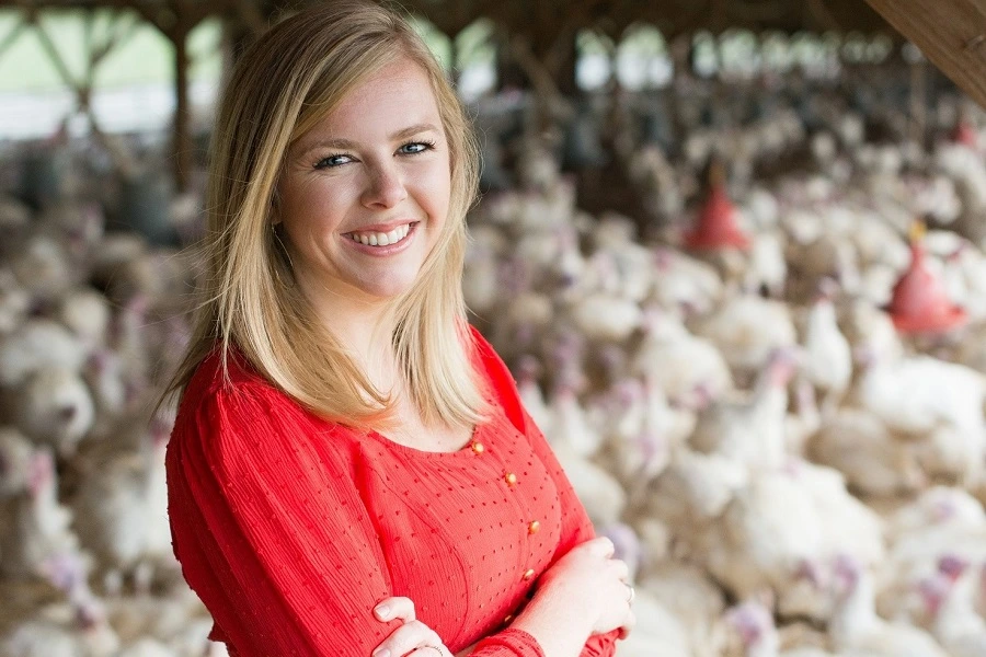 a young woman in red sweater with blonde hair smiling at a turkey farm with birds behind her